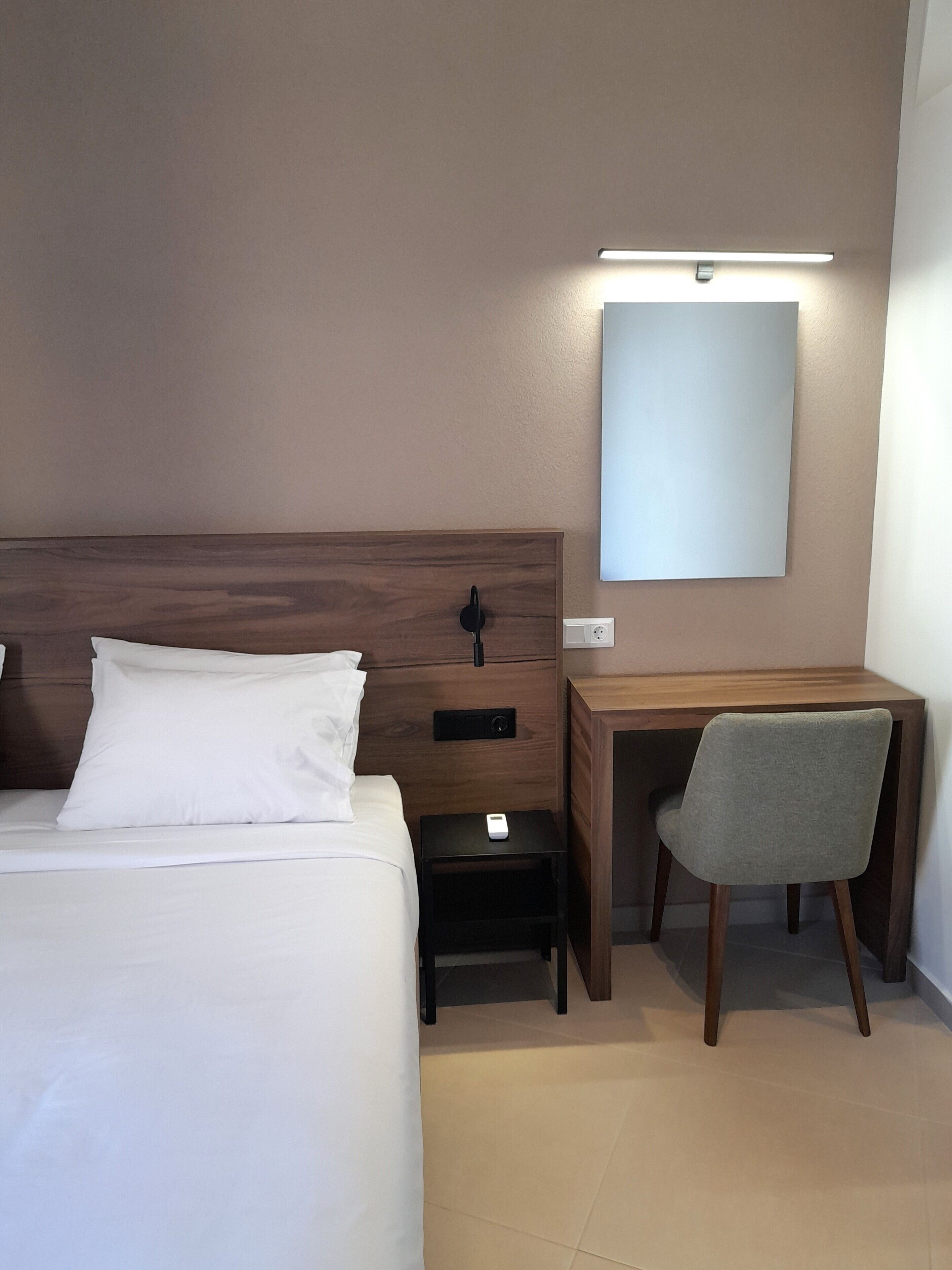 Une chambre d’hôtel équipée d’un lit, d’une table de chevet, d’un bureau, d’une chaise et d’une lampe fixée au mur.