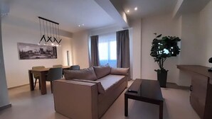 Una sala moderna con sofá, mesa de comedor y sillas. Hay una planta grande en maceta y un escritorio con una computadora.