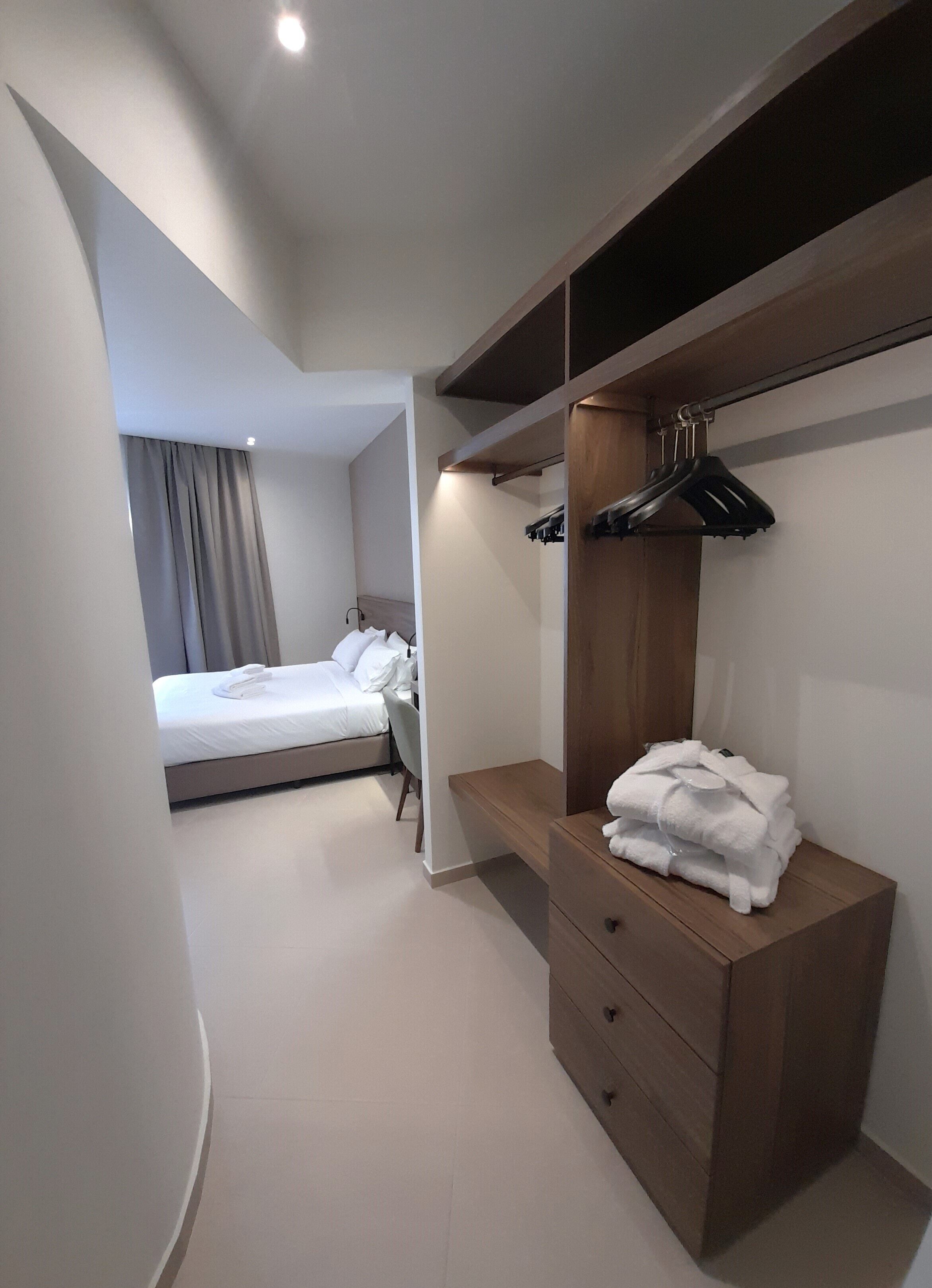 Una habitación de hotel moderna con una cama, un aparador de madera con cajones, un banco y un perchero.