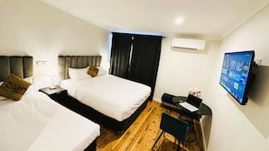A hotel room with two beds, a desk with a chair, a flat-screen TV, and an air conditioning unit. - Seven Inn (Gumly Gumly)