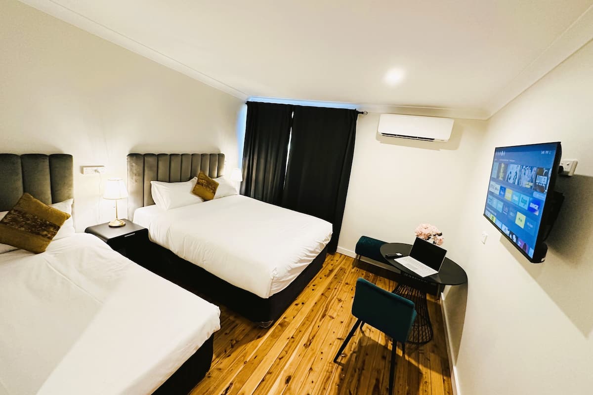 A hotel room with two beds, a desk with a chair, a flat-screen TV, and an air conditioning unit.