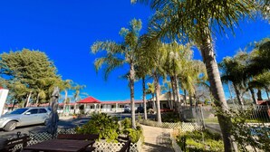 A parking area with a red-roofed building, palm trees, and a clear blue sky. - Seven Inn (Gumly Gumly)