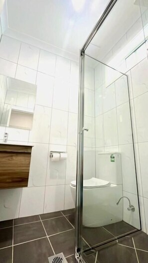 A modern bathroom with a glass shower enclosure, white tiled walls, a wooden vanity, and a toilet.