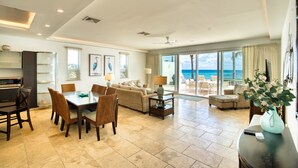 A spacious living area with a dining table, chairs, and a sofa. There is a view of the ocean through large windows.