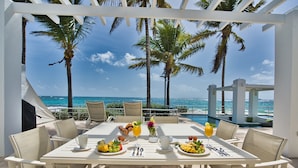 A dining table set for six with a view of the ocean and palm trees.