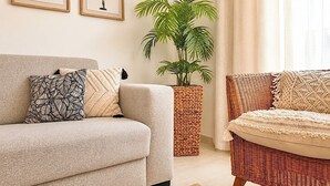 Ein Wohnzimmer mit einer Couch, zwei Kissen, einer Topfpflanze und einem Korbstuhl.