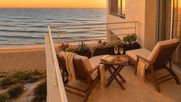 Ein Balkon mit Blick auf den Ozean, Holzmöbel und ein Tisch mit einem Buch und Gläsern.