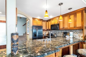 A kitchen with granite countertops, stainless steel appliances, wooden cabinets, and pendant lighting.