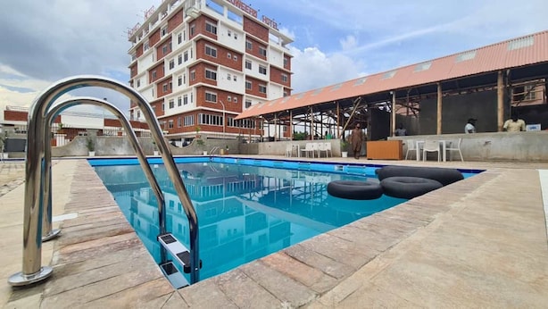 Piscina com escada de metal, rodeada por ladrilhos de pedra.