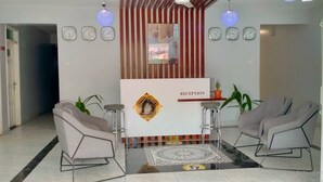 Uma área de recepção com balcão, duas poltronas, tapete estampado e relógios de parede.