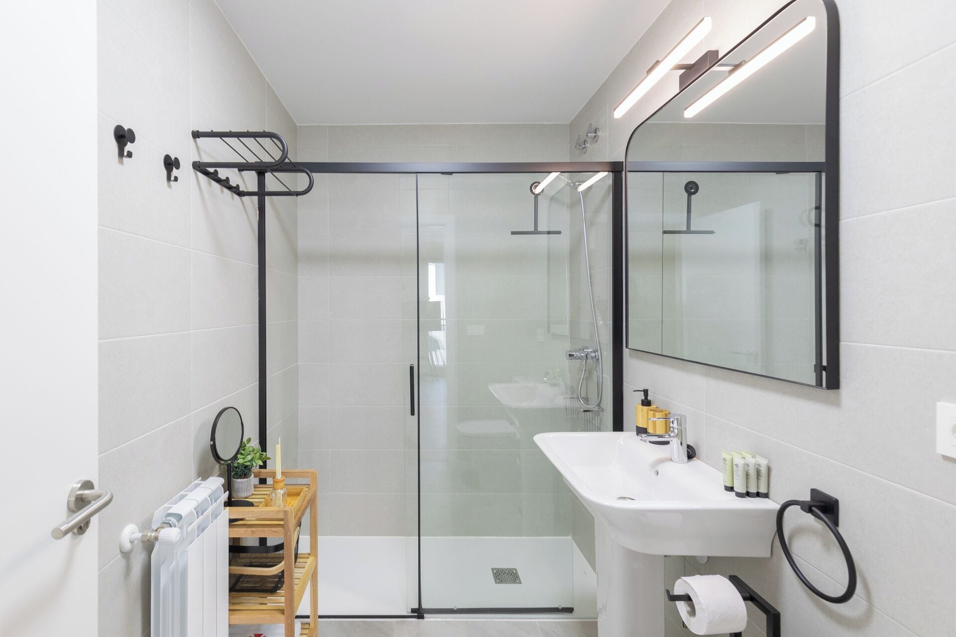 A modern bathroom with a glass shower enclosure, a white sink with toiletries, and a mirror.