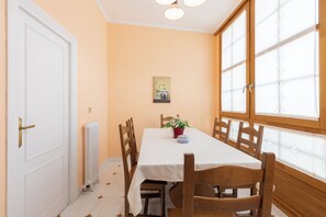 Un coin repas avec une table dressée pour quatre personnes, des chaises en bois, une nappe blanche, une plante en pot et un tableau accroché au mur.
