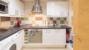 Een kleine keuken met witte kastjes, een roestvrijstalen afzuigkap, een magnetron, een spoelbak en een vaatwasser.
