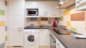 Een compacte keuken met witte kastjes, een magnetron, een wasmachine en een fornuis.