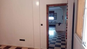 Una habitación con piso a cuadros, una puerta que da a otra habitación y un interruptor de luz visible en la pared.