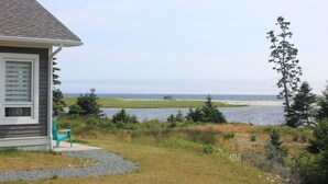 A house with a view of the ocean and a grassy area with a chair. - Cottage at Cherry Hill Beach (Cherry Hill)