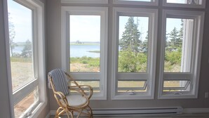 A room with large windows overlooking a body of water and greenery. - Cottage at Cherry Hill Beach (Cherry Hill)