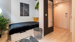 A modern room with a bed, a small round table, a wall-mounted plant, and a door leading to another room. - RentPlanet - Apartamenty Dyrekcyjna (Wroclaw)