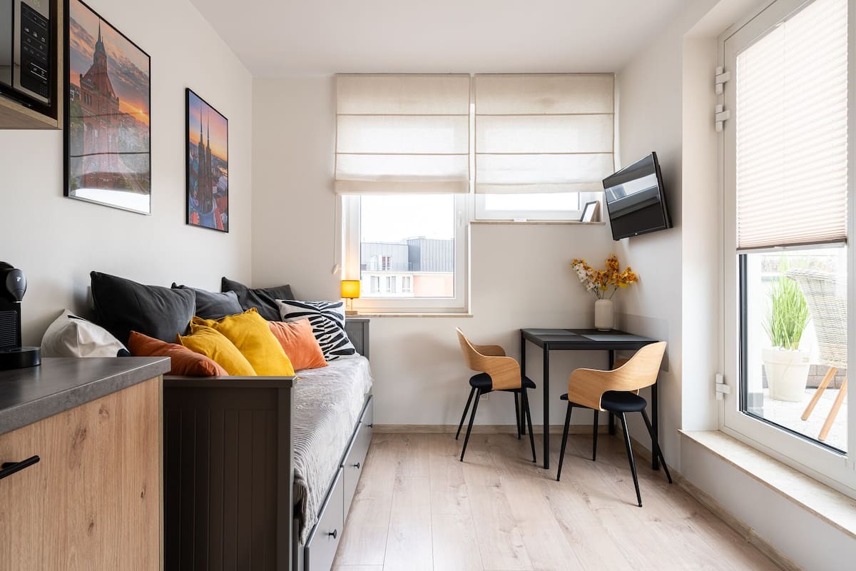 A compact room with a bed, a desk, two chairs, a TV, and artwork on the walls.