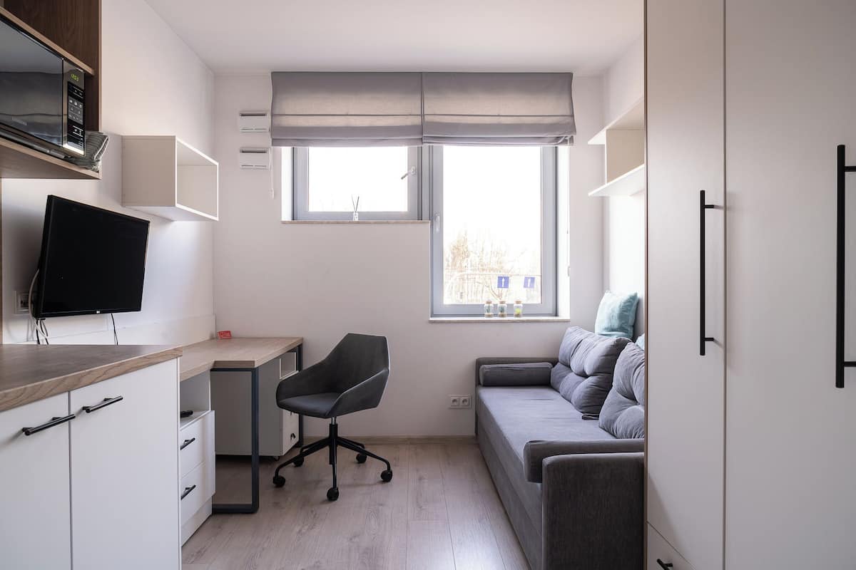 A compact bedroom with a bed, a desk, a chair, and a TV.