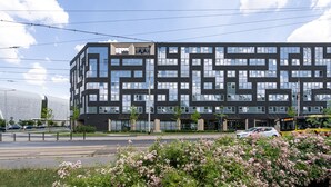 A modern building with a geometric facade, multiple windows, and a street in front with a bus and cars. - RentPlanet - Apartamenty Dyrekcyjna (Wroclaw)