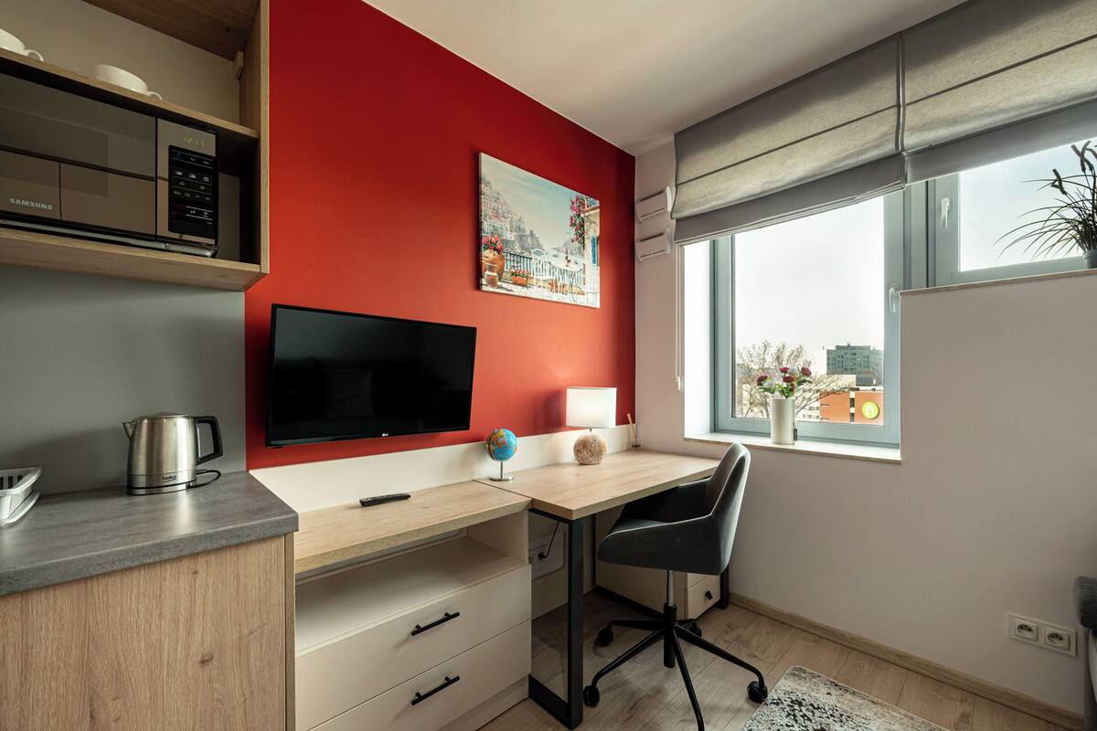 A modern kitchen with a microwave, a kettle, and a flat-screen TV on the wall.