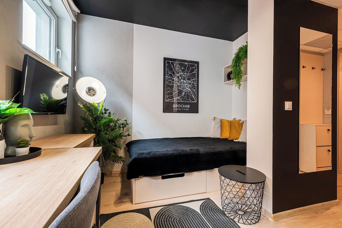 A modern bedroom with a bed, a desk, a mirror, and a wall-mounted artwork.