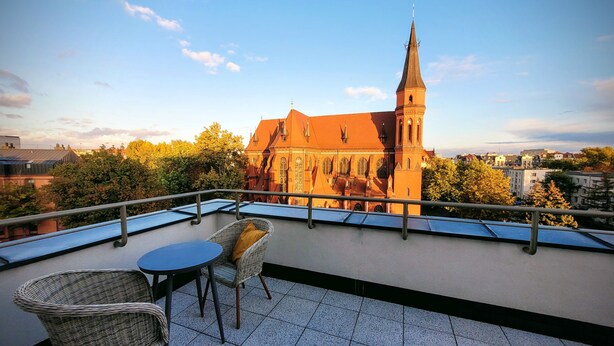 A balcony with a table and chairs overlooking a historic church with a tall tower. - RentPlanet - Apartamenty Dyrekcyjna (Wroclaw)