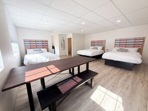 A modern hotel room with two beds, a large wooden table, and a bench.