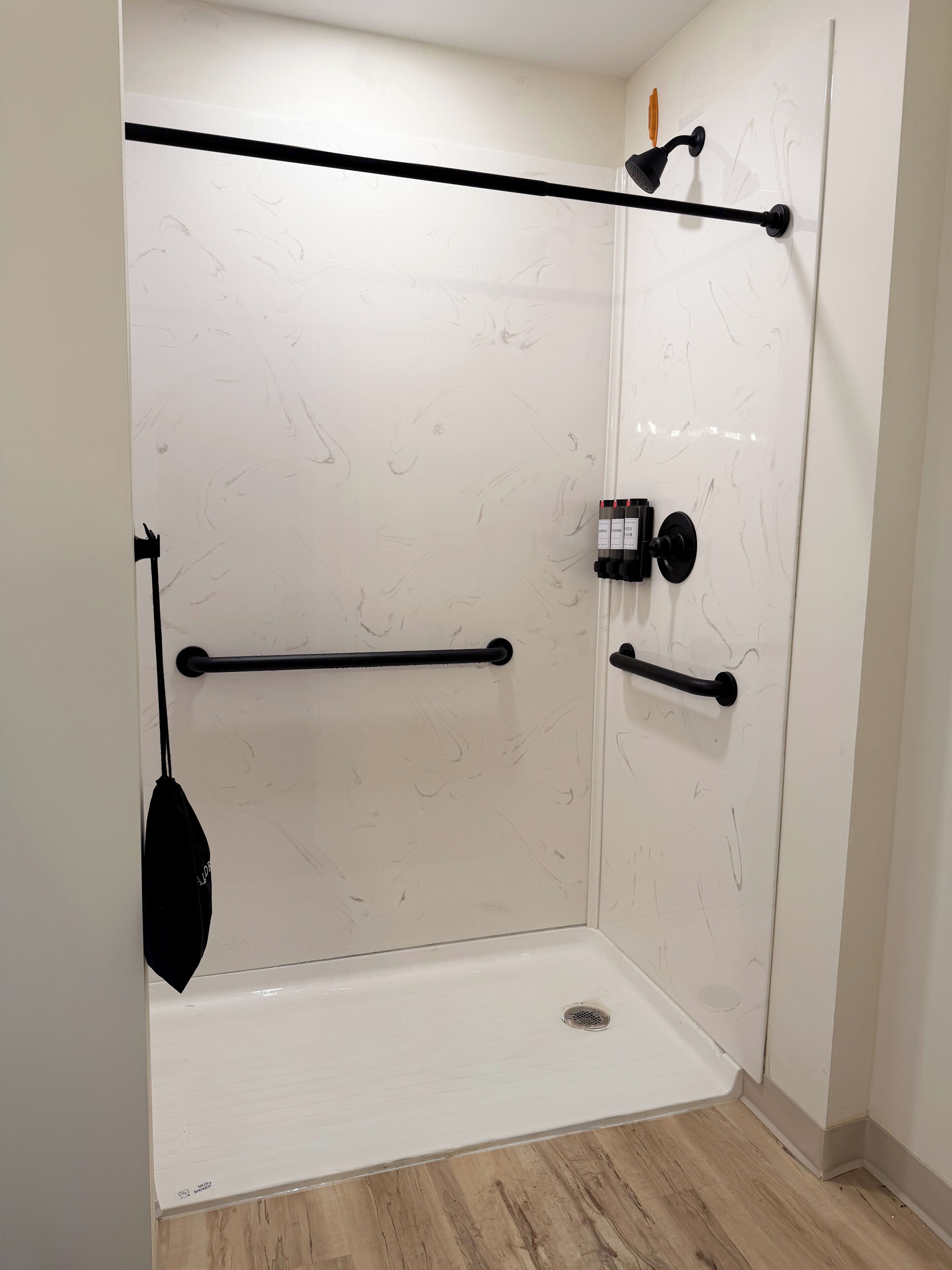 A shower enclosure with a black towel rack, a black towel, and a black shower head.