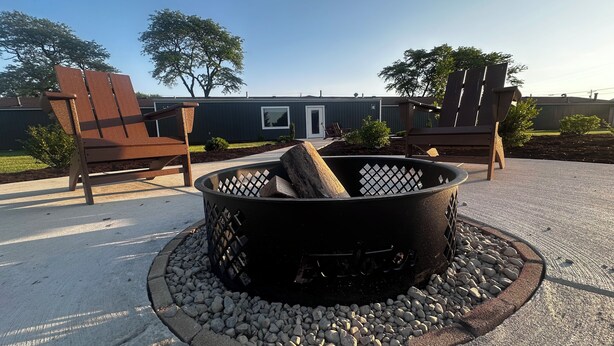 A fire pit with logs, surrounded by a stone border and rocks, with two wooden chairs facing it. -  Explorer Rest & Recreation (Sandusky)