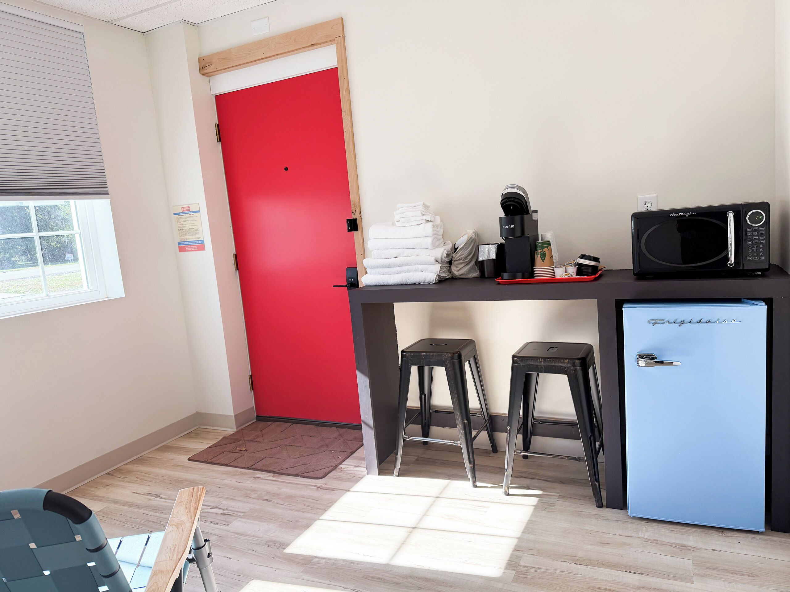 A kitchenette with a red door, a black microwave, a coffee machine, and a blue mini-fridge.