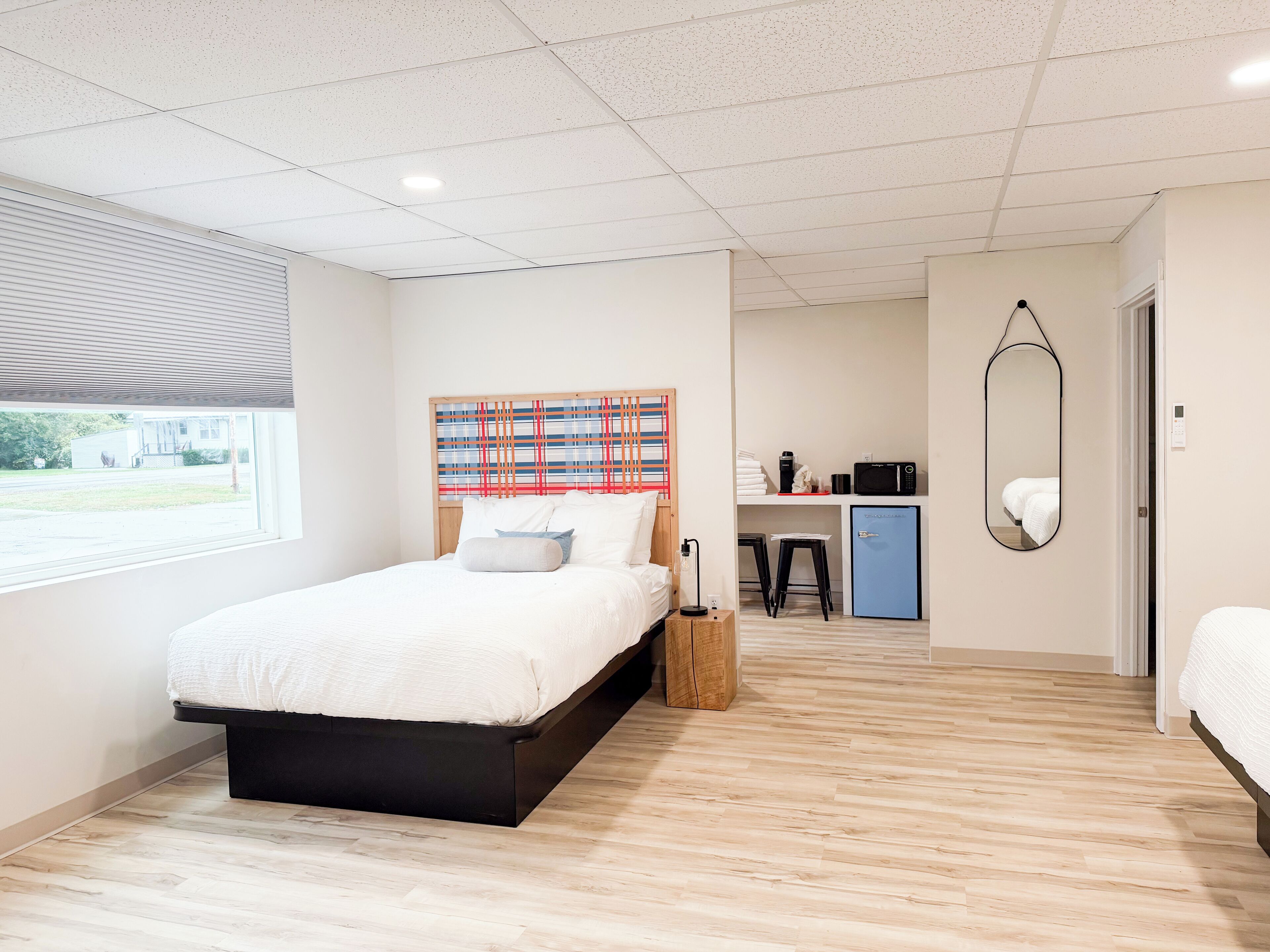 A modern bedroom with a large bed, a desk with a computer, and a small kitchenette.