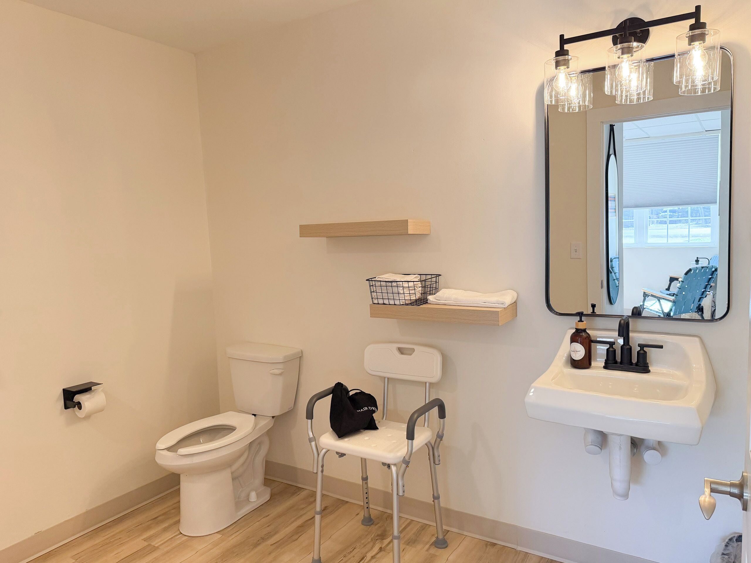 A modern bathroom with a toilet, a sink with a mirror, a walking aid, and a shelf with towels.