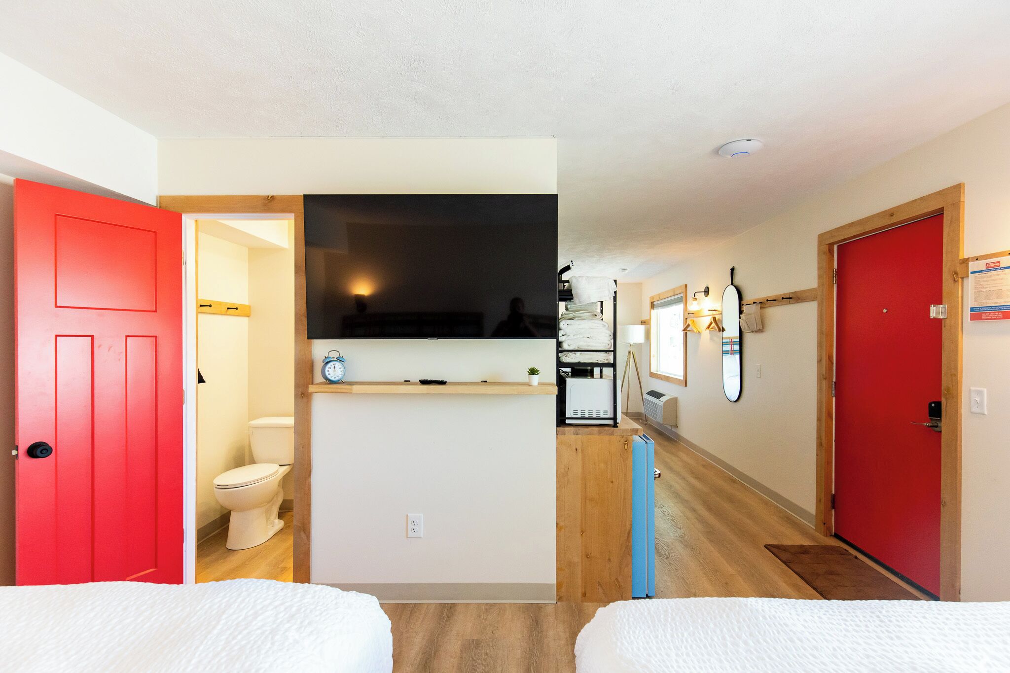 A hotel room with a red door, a white toilet, a small kitchenette, and a wooden floor.