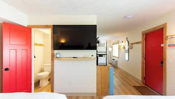 A hotel room with a red door, a white toilet, a small kitchenette, and a wooden floor.