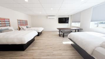 A hotel room with two beds, a TV, a table, and a window with blinds.
