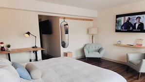 A modern hotel room with a large bed, a desk with a lamp, a television, and a seating area with two chairs. -  Explorer Rest & Recreation (Sandusky)