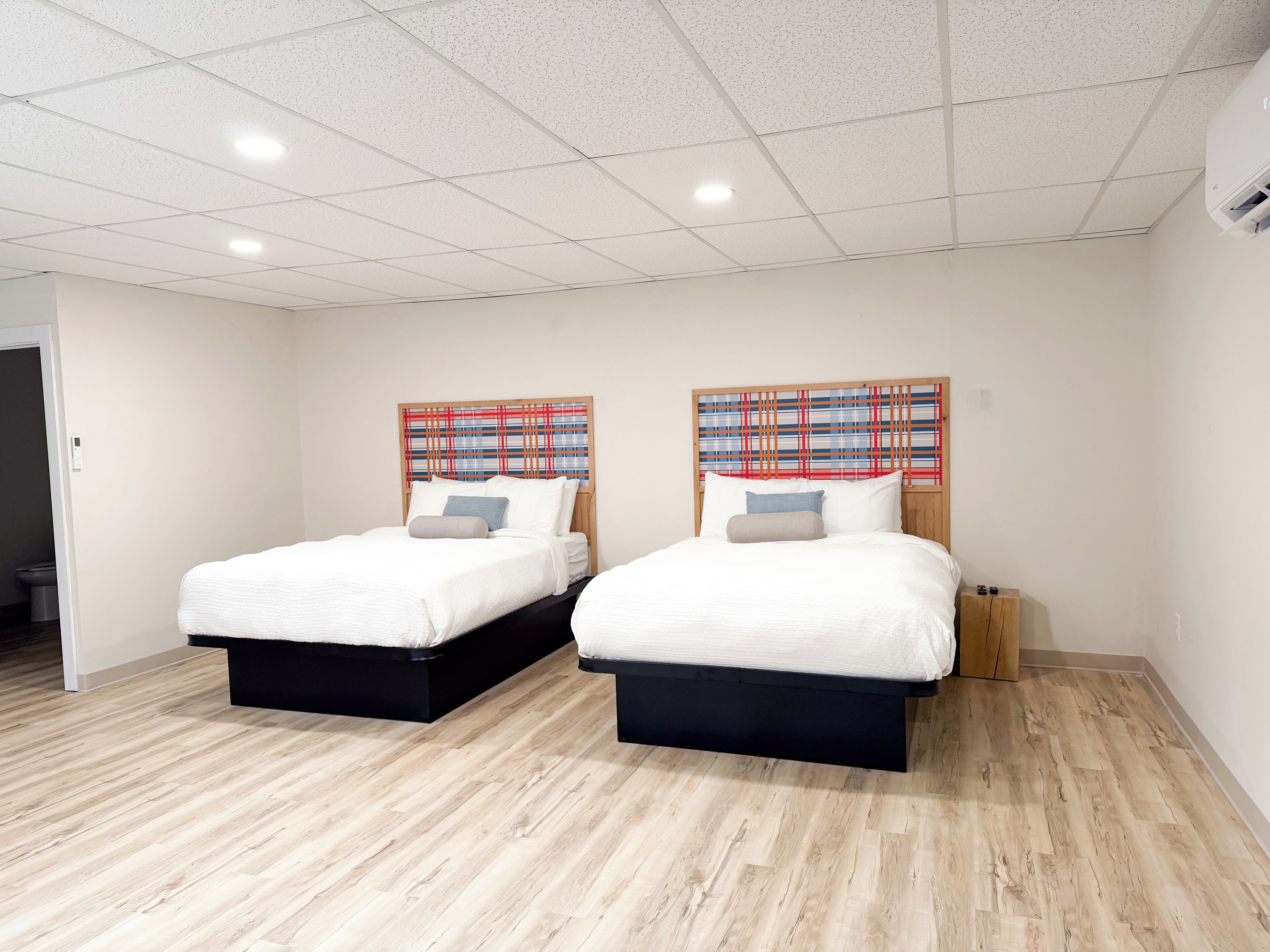 A hotel room with two beds, a wooden headboard, and a light-colored wooden floor.