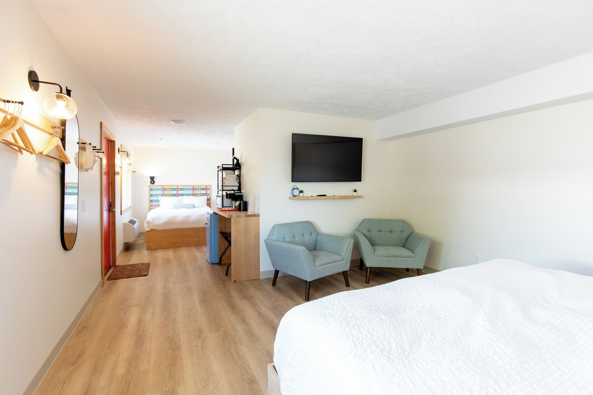 A hotel room with a bed, two armchairs, a desk with a computer, a flat-screen TV, and a small shelf.