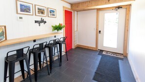 A reception area with a wooden counter, black bar stools, framed pictures on the wall, a red door, and a 'hello' mat at the entrance. -  Explorer Rest & Recreation (Sandusky)