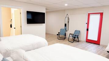 Quarto de hotel com duas camas, uma televisão, um espelho, duas cadeiras e uma porta vermelha.