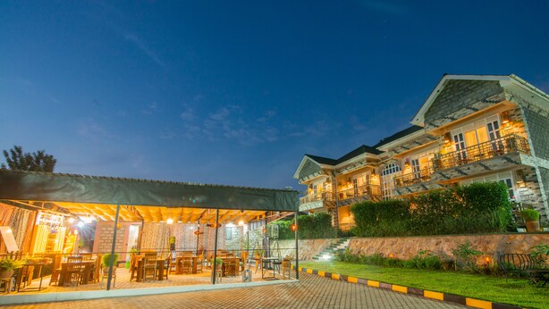 A well-lit outdoor seating area with tables and chairs, a covered section, and a stone building with a balcony in the background. - Jet Villas Entebbe (Entebbe)