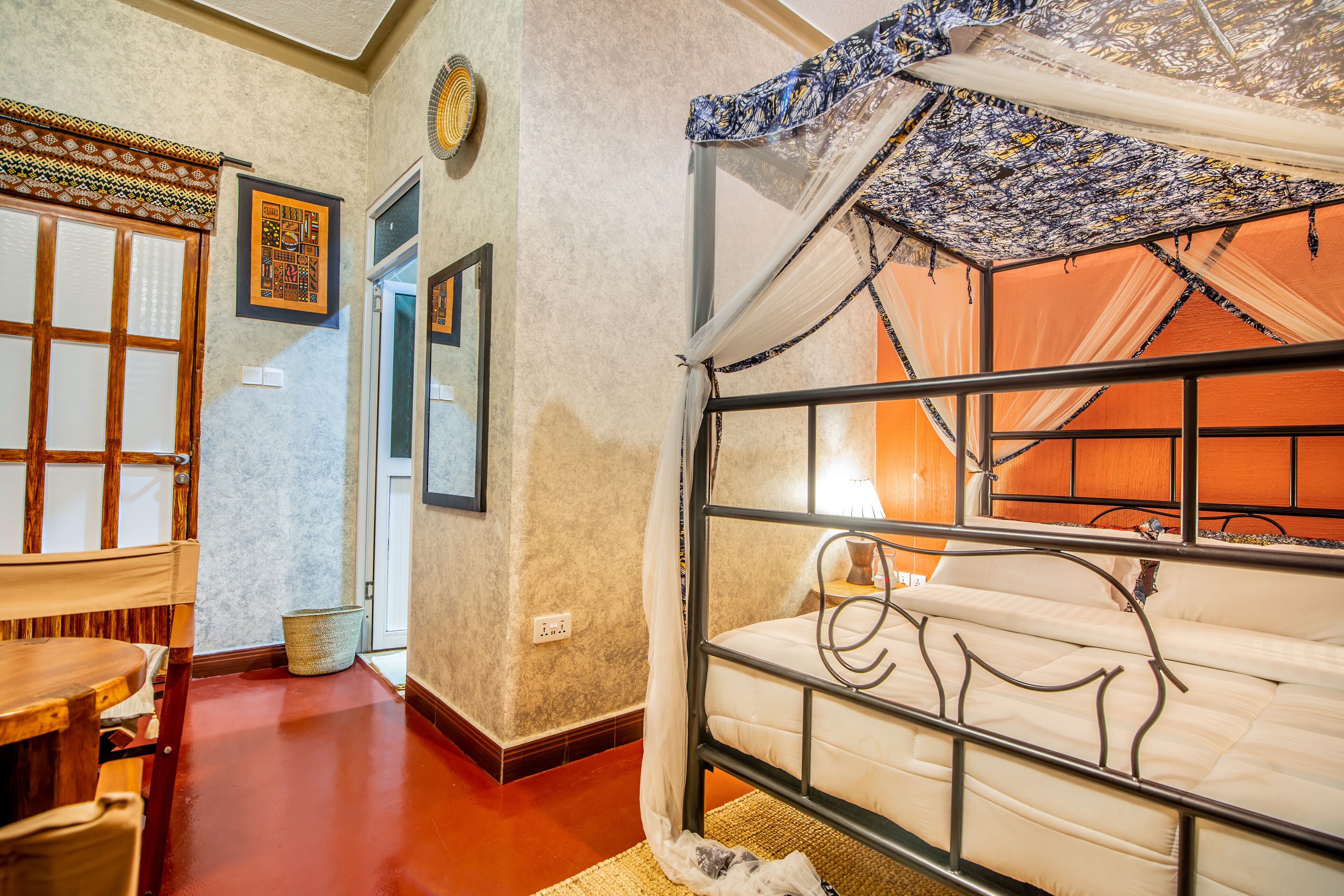 A room with a bed, a chair, a small table, and a wall with framed pictures.