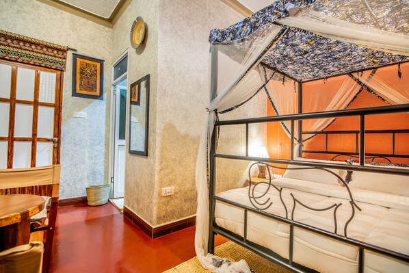 A room with a bed, a chair, a small table, and a wall with framed pictures.