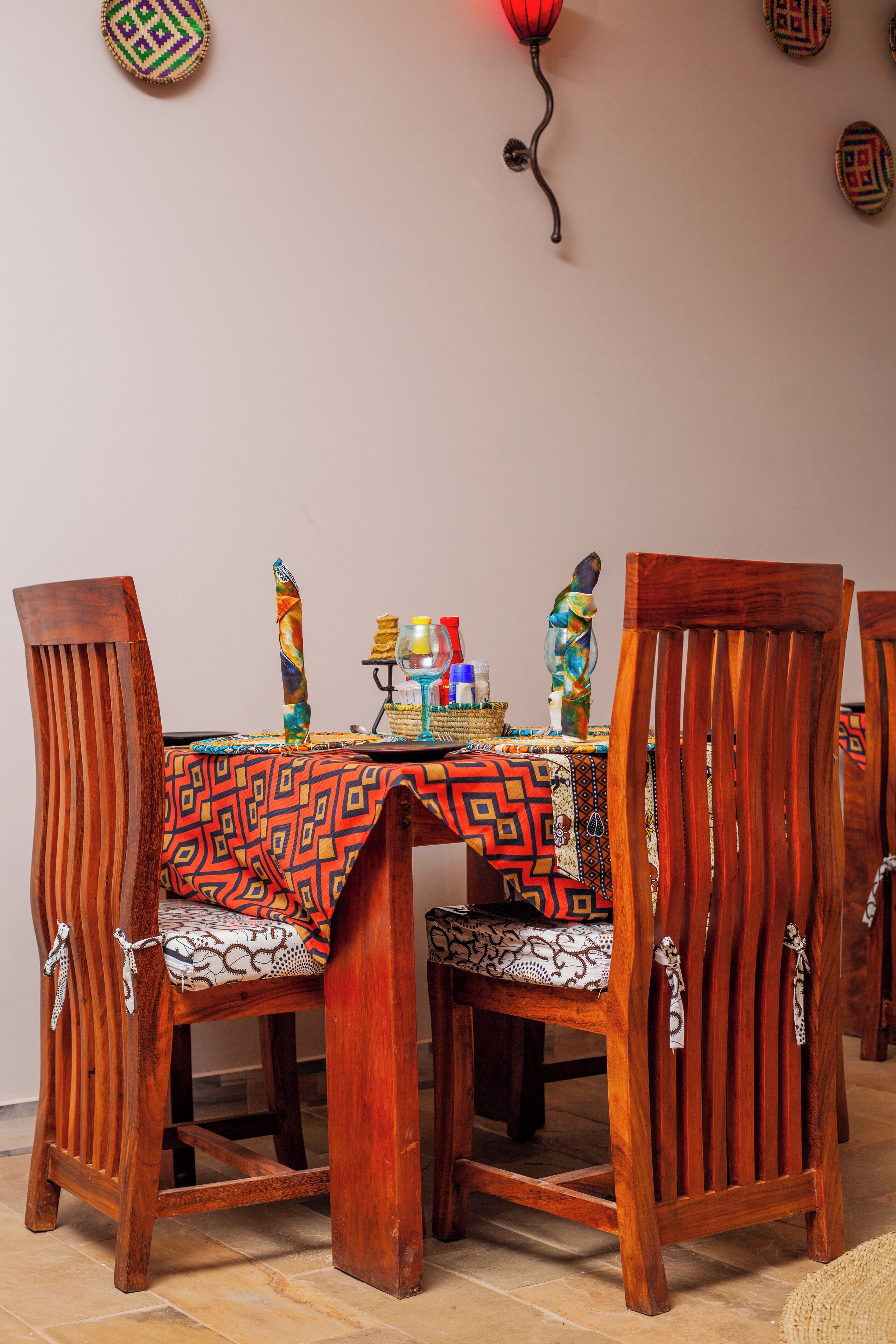 A dining table with a colorful tablecloth, surrounded by wooden chairs with intricate designs.