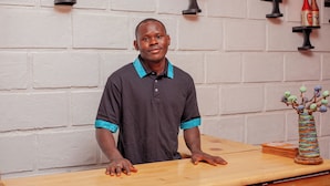A man standing behind a wooden counter with a decorative vase and some items on it. - Jet Villas Entebbe (Entebbe)