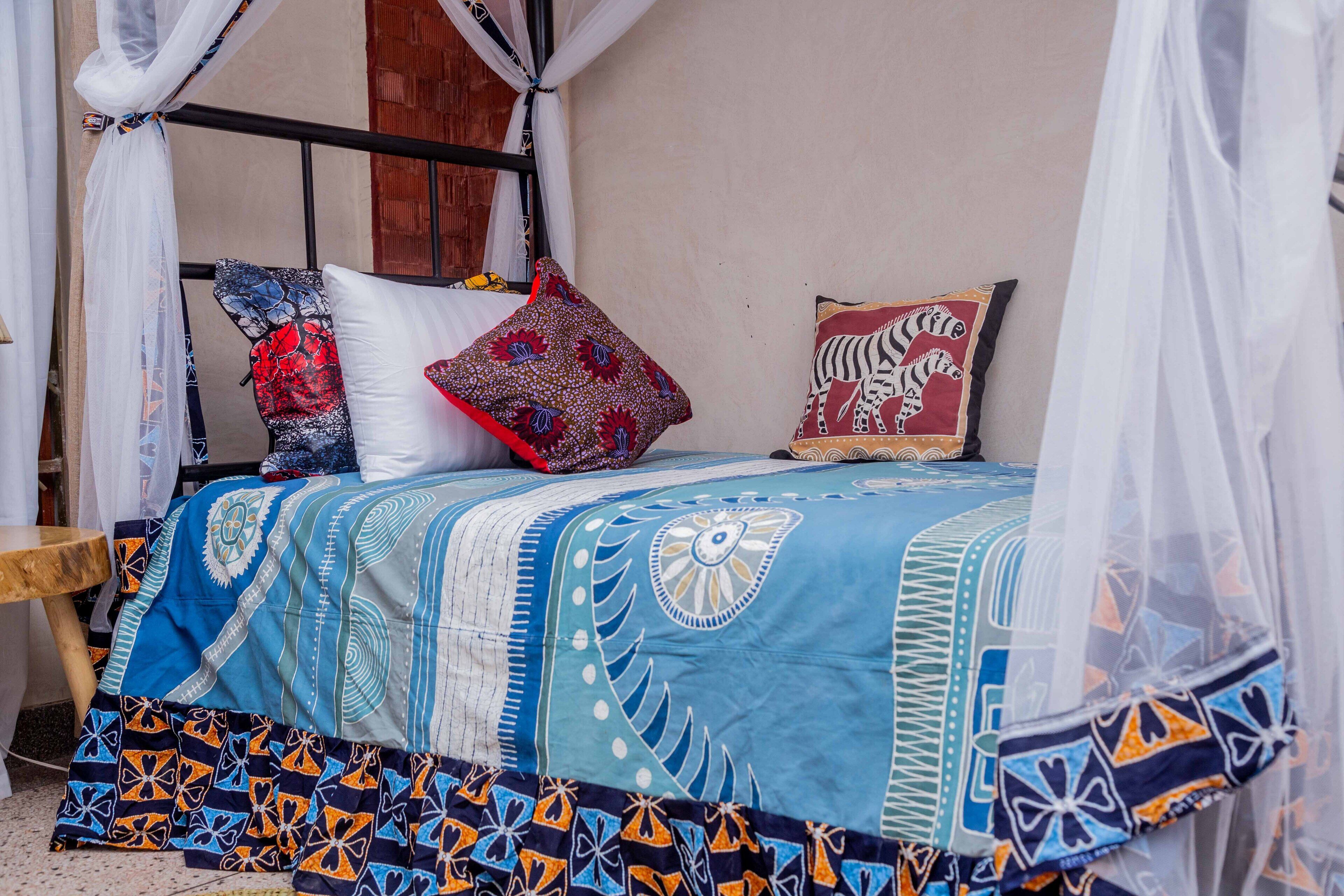 Een bed met een blauw-wit beddegoed, twee kussens met rode en zebra accenten, en een houten nachtkastje.