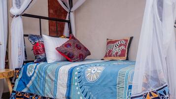 Een bed met een blauw-wit beddegoed, twee kussens met rode en zebra accenten, en een houten nachtkastje.