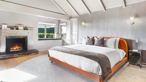 A spacious bedroom with a large bed, a fireplace, and a view of the outdoors.